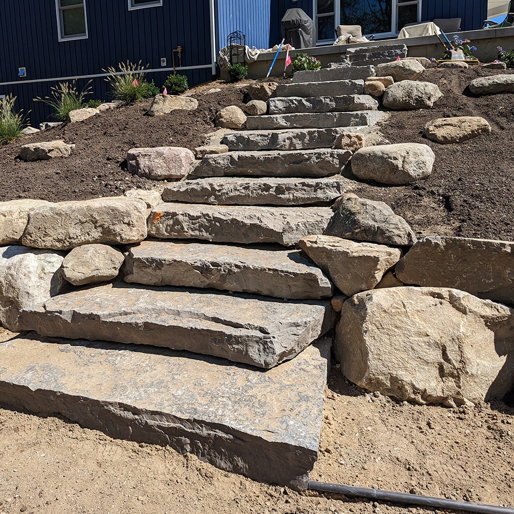 Image by Bladerunner’s of stone boulders being installed as steps up a steep hill.