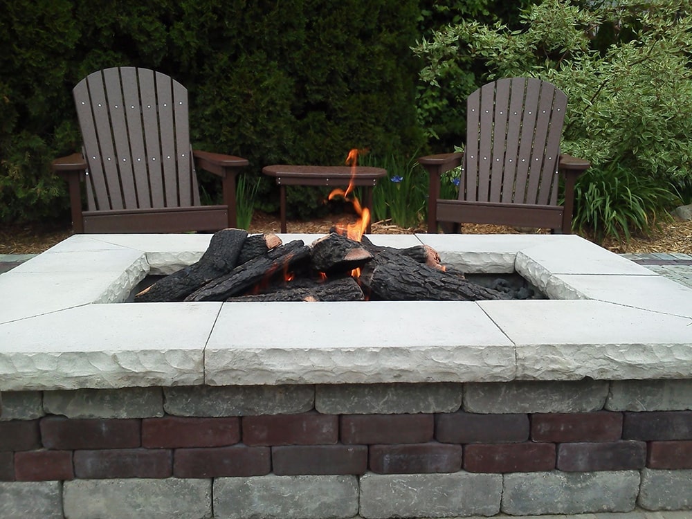 Close-up image of an outdoor lit gas fire pit, constructed by BladeRunners Landscaping.