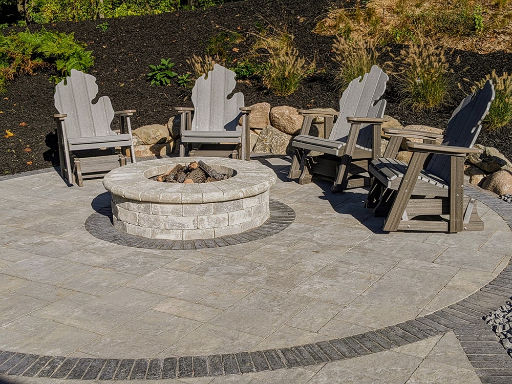 Image of an outdoor patio with a gas fire pit, surrounded by MI-shaped  Adirondack chairs, completed by BladeRunners Landscaping.