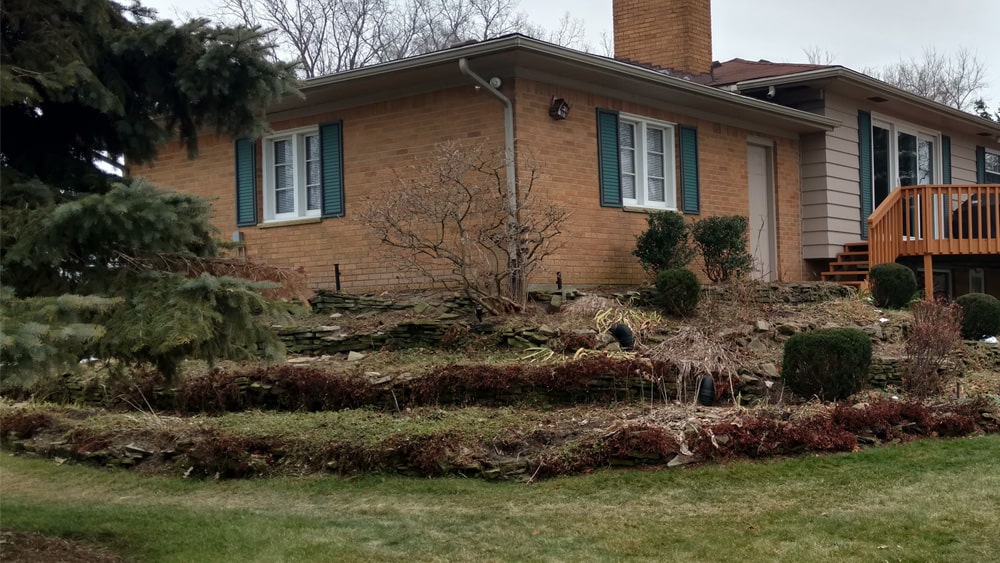 Before: Side view of the same dated home and landscaping, with a disheveled retaining wall.